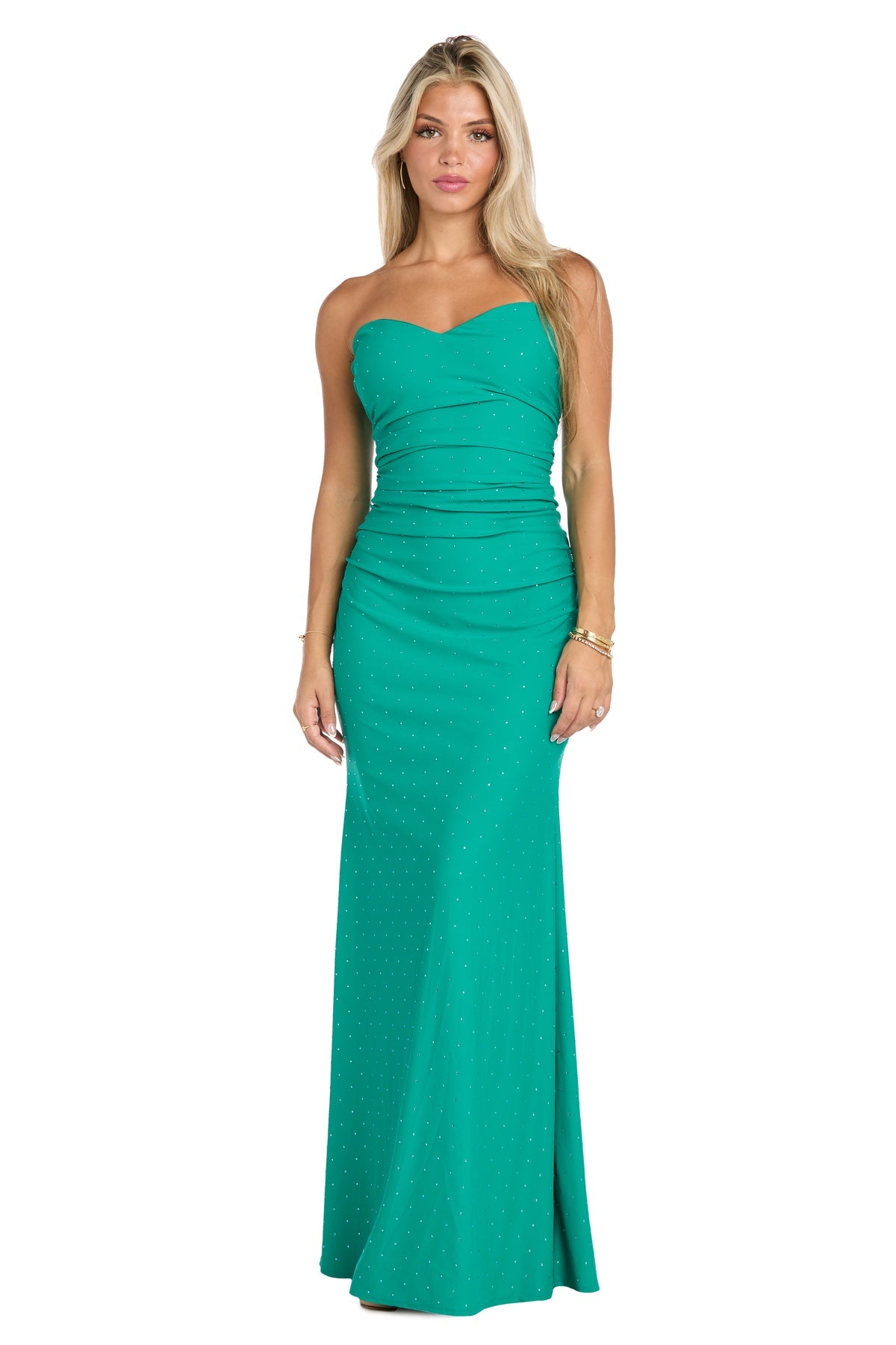 A woman stands wearing the Jade Green Long Ruched Prom Dress: Morgan 19016—strapless, fitted, floor-length with subtle dot patterns—paired with gold bracelets on one wrist.